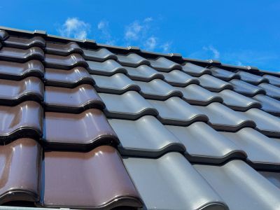 Dachziegel in Braun und Grau installiert unter blauem Himmel, zeigt Auswahl an Materialien f&uuml;r Dachdeckung