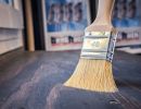 Pinsel Gr&ouml;&szlig;e 40 streicht dunkles Holz, Hintergrund zeigt unscharfe Poster &ndash; Szene aus Malerbereich