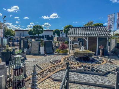 Gartencenter zeigt Pflastersteine, Brunnen und Dekoartikel im Au&szlig;enbereich unter klarem Himmel