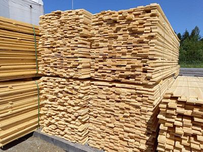 Gestapelte Holzbretter drau&szlig;en bei Sonne, ordentlich geb&uuml;ndelt f&uuml;r Transport oder Verkauf im Baustoffhandel.