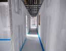 Langer Rohbauflur mit unverputzten W&auml;nden und freiliegenden Kabeln an der Decke, zeigt Innenausbauphase.