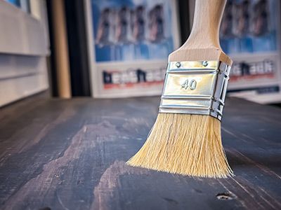 Ein Pinsel tr&auml;gt Lasur auf Holz auf &ndash; zeigt die Veredelung und den Schutz von Holzoberfl&auml;chen im Handwerksbereich