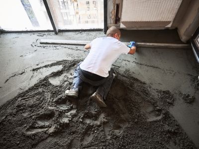 Person gl&auml;ttet frischen Betonboden mit langer Latte, ebene Fl&auml;che entsteht durch pr&auml;zises Ausrichten im Innenraum