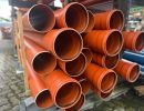 Gestapelte orange Kunststoffrohre lagern drau&szlig;en, zeigen Materialien f&uuml;r unterirdische Infrastrukturprojekte