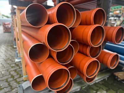 Gestapelte orange Kunststoffrohre lagern drau&szlig;en, zeigen Materialien f&uuml;r unterirdische Infrastrukturprojekte