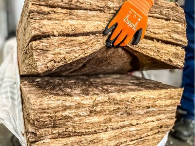 Person mit Handschuhen h&auml;lt dicke D&auml;mmmatte, zeigt thermische Isolierung mit Mineralwolle oder Glasfaser
