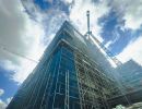Hohes Geb&auml;ude einger&uuml;stet, Kr&auml;ne arbeiten daran, zeigt Fortschritt im Hochbau unter blauem Himmel mit Wolken